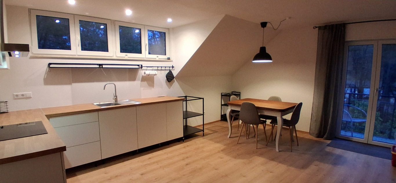 Moderne Küche mit Holzoberflächen, Esstisch und Fenster mit Blick ins Freie.