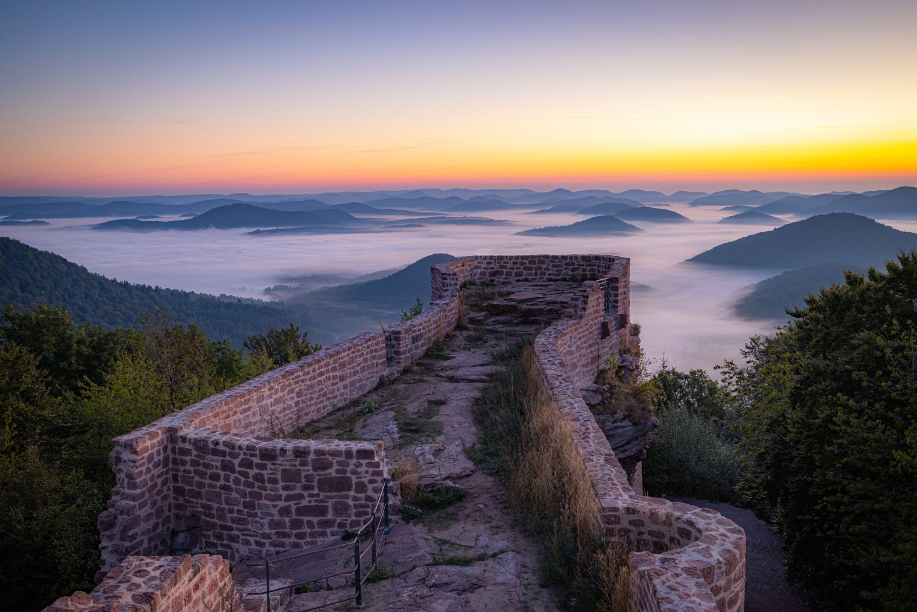 Wegelnburg Blick von einer Burgruine auf eine neblige Landschaft bei Sonnenaufgang.